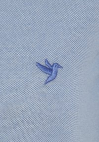 Hele sinine tekstureeritud kangas, millel on vasakul küljel väike, tikitud tume sinine kolibri logo.