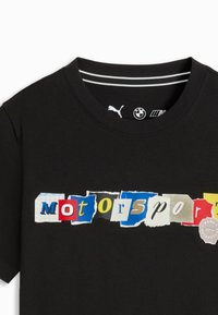 T-shirt noir avec le mot "motorsport" écrit en lettres multicolores style papier déchiré sur le devant, avec les logos Puma et BMW à l'intérieur du col.