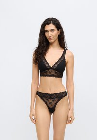 Conjunto de lingerie preta em renda com um bralette de decote em V e detalhes florais transparentes, combinado com uma tanga em renda transparente a condizer.