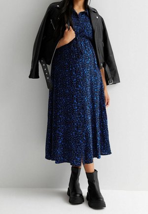 Blauwe maxi-jurk met bloemenprint en korte mouwen, gecombineerd met een aangesloten zwarte leren jas en stevige zwarte enkellaarsjes.