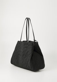 Black quilted tote bag featuring a floral pattern, two long handles, and a soft, textured material. The design is spacious and angular.