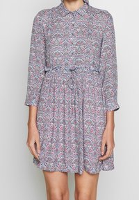 Blumenmuster-Kleid mit Kragen, langen Ärmeln und tailliertem Schnitt. Die Farben umfassen Rosa, Blau und Weiß auf einem hellen Hintergrund.