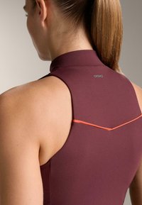 Bordó sportfelső magas gallérral, narancssárga díszítő vonallal a hátán. Simább, rugalmas anyag a kényelemért és a jó illeszkedésért.