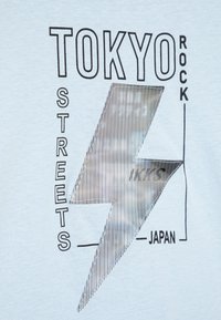 Hellblaues T-Shirt mit schwarzem Text und einem reflektierenden Blitzdesign. Der Text umfasst "TOKYO", "STREETS" und "JAPAN."