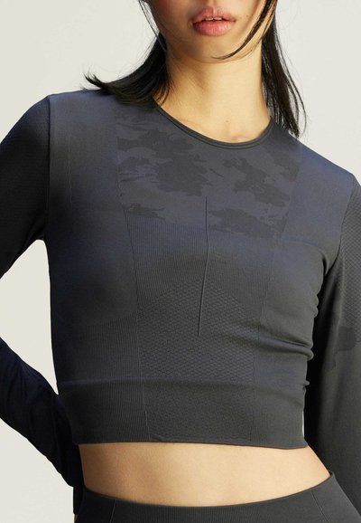 Langarm, cropped top in donkergrijs met textuurpatronen, gladde stof en een ronde halslijn met contrasterende paneeldetails.