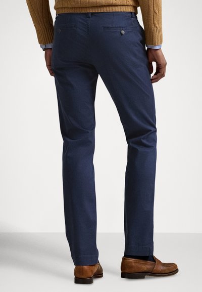 Granatowe chinosy wykonane z bawełny, o prostym kroju nogawki, z dwoma tylnymi kieszeniami zapinanymi na guziki, w połączeniu z brązowymi mokasynami.