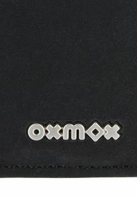 Surface noire texturée avec des lettres métalliques argentées formant le mot « o x m o x » près du bord inférieur.