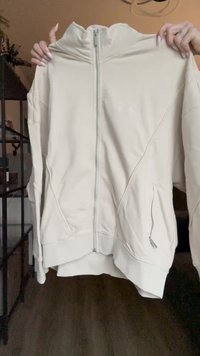 Sudadera con cremallera de color beige claro, hecha de tela suave, con alto cuello, bolsillos laterales y dobladillo acanalado, con un diseño minimalista y costuras.