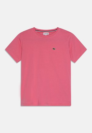Różowy t-shirt z krótkim rękawem i okrągłym dekoltem z małym zielonym logo krokodyla Lacoste na lewej piersi.