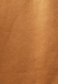 Gros plan sur un tissu marron texturé avec un motif de tissage diagonal, montrant la structure détaillée des fils et des ombres subtiles.