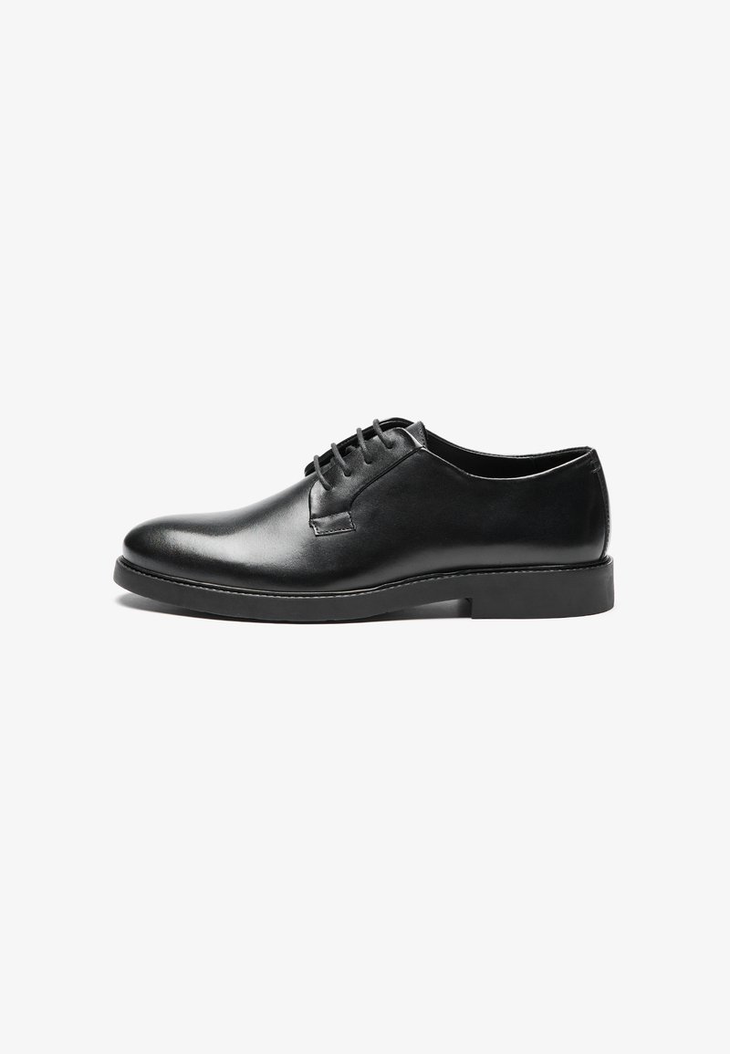 Zapato negro de piel con cordones, con punta redondeada, textura suave, costuras mínimas y un tacón bajo de goma para mayor estabilidad.