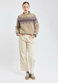 Beige gebreide trui met kleurrijke geometrische patronen, gecombineerd met crèmekleurige wijde broek en bruine sneakers met witte veters.