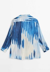 Niebiesko-kremowa koszula na guziki z abstrakcyjnym, rozmytym wzorem. Długie rękawy z kontrastującymi mankietami, lekka tkanina, kołnierzyk przy szyi.