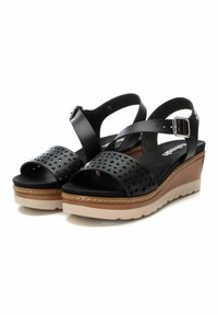 Sandalias de cuña negras con parte superior perforada, correa ajustable en el tobillo y suela de color claro contrastante. El diseño texturizado realza el interés visual.