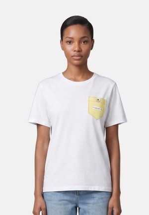 Giovane donna che indossa una T-shirt bianca a maniche corte con una tasca sul petto gialla con bottoni etichettata "FRESH" e jeans azzurri chiari.