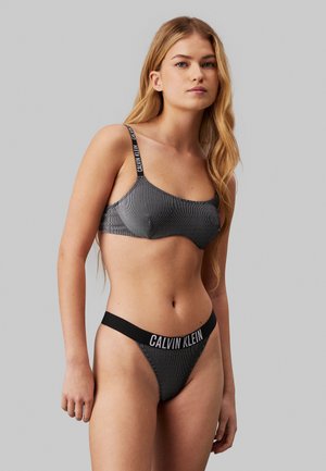 Black and white striped bralette with adjustable straps and black waistband featuring "CALVIN KLEIN" logo on the front.