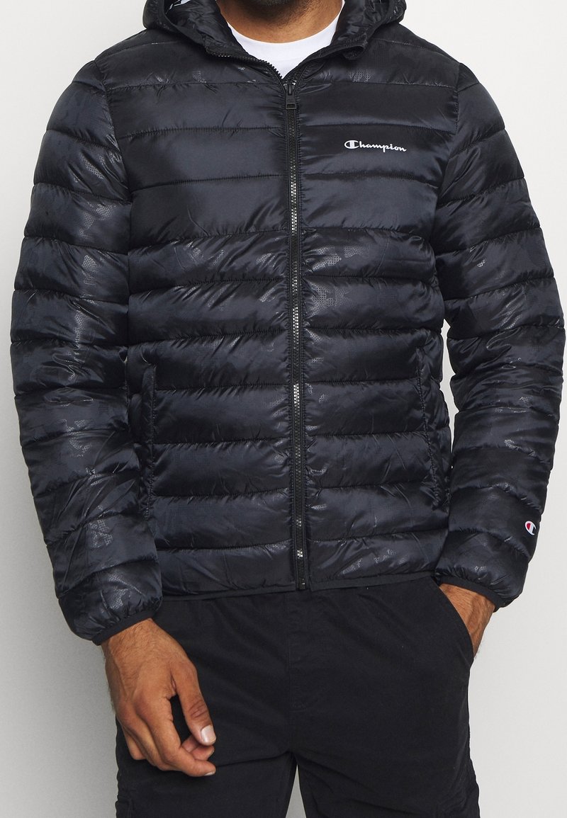 Czarna kurtka puchowa z zamkiem z przodu, elastycznymi mankietami i kapturem. Posiada przeszywane panele oraz małe logo na piersi. Miękki, błyszczący materiał.
