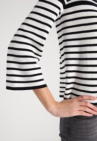 Haut à rayures noires et blanches avec manches trois quarts, tissu doux et coupe décontractée, associé à un jean gris ajusté.