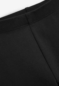 Svarta leggings med en slät, texturerad yta och ett brett elastiskt midjeband, med platta sömmar och minimal detaljer på tyget.