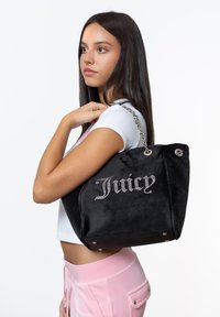 Zwarte suède tote bag met een zilveren kettinghandvat, voorzien van "Juicy" versierd met rhinestones. Gestructureerde vorm met drukknoopsluiting en metalen accenten.