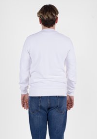 Felpa bianca a maniche lunghe con colletto e polsini a costine, abbinata a jeans in denim blu con tasche posteriori e finitura testurizzata.