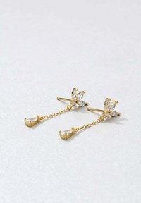 Goldene Tropfohrringe mit floralem Design, die klare Edelsteine und zarte Ketten aufweisen, die birnenförmige Anhänger am Ende verbinden.