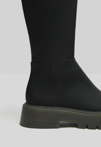 Bottine noire à finition mate lisse, semelle en caoutchouc robuste et détails de couture subtils. Design légèrement épais avec des orteils arrondis.