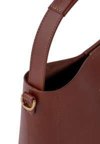 Brown leather handbag with a smooth finish, featuring a structured shape, elongated strap, and gold-tone hardware accents.