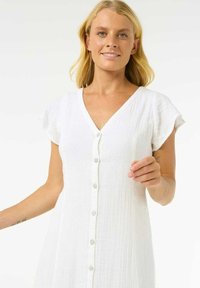 Robe blanche avec décolleté en V, manches courtes à volants et fermeture à boutons. Le tissu texturé offre un aspect respirant.