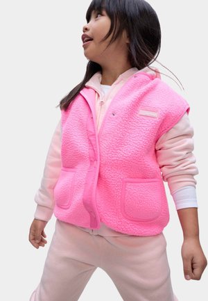 Roze fleecevest met een gestructureerde afwerking, voorzien van een sluiting aan de voorkant, twee zakken en een merklabel. Draagt over een lichtroze sweatshirt.