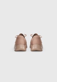 Bruine sportieve schoenen met een gestructureerd bovenwerk, ronde hak en veters. De zool is iets dikker, wat zorgt voor demping en ondersteuning.