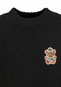 Zwarte gebreide trui met een gestructureerde afwerking en een grote geborduurde berenpatch in bruin, die een gecamoufleerde hoed en shirt draagt.