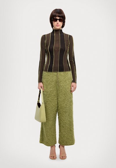 Haut à manches longues rayé noir et marron associé à un pantalon large texturé vert et un petit sac à main vert. Le mannequin porte des lunettes de soleil noires.