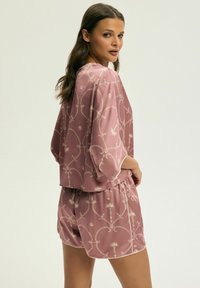 Zestaw odzieży domowej z jedwabiu w odcieniu przykurzonego różu, składający się z krótkiej, prostokątnej bluzki z szerokimi rękawami oraz wzorzystych szortów. Złote akcenty w kwiatowym wzorze zdobią całość.