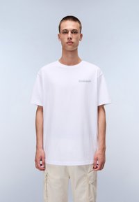 Vit bomulls-t-shirt med rund halsringning och korta ärmar, med en liten logotyp på vänster bröst. Mjuk textur och ledig passform.