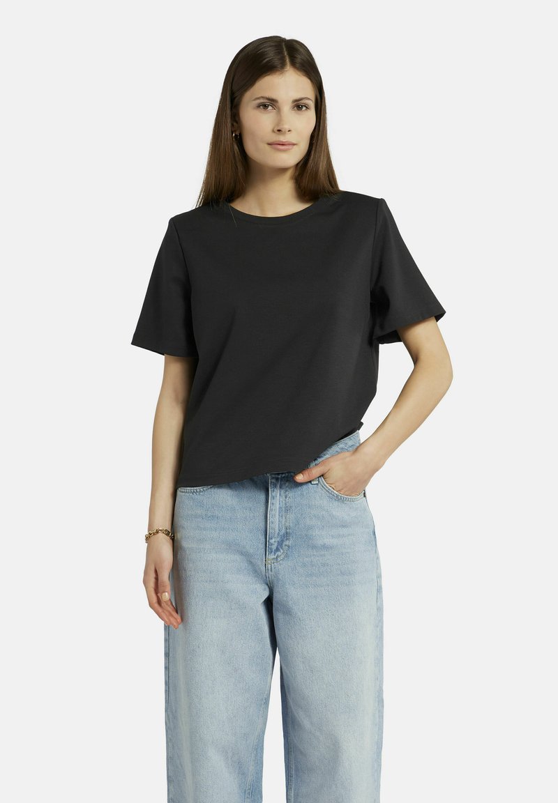 Schwarzes Baumwoll-T-Shirt mit Rundhalsausschnitt und kurzen Ärmeln, kombiniert mit hellblauen High-Waist-Jeans. Glatte Textur, lockere Passform.
