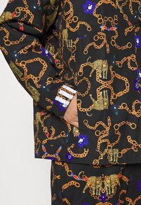 Svart jacka med en guldcancer och leopardmönster, med färgglada blommönster och randig manschettdetalj.