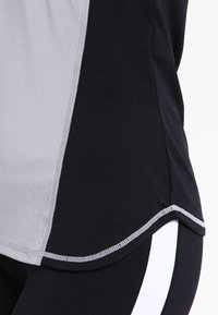 Gros plan d'un haut de sport noir et gris avec un ourlet arrondi sur un legging noir avec une bande verticale blanche.