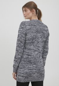 Long gilet en tricot gris et noir avec un motif texturé, des poignets côtelés et un ourlet droit, conçu pour une coupe décontractée.