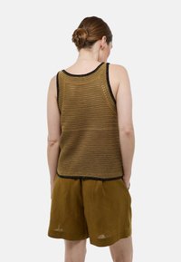 Débardeur en maille ouverte, marron, avec des bords noirs. Porté avec un short large marron. Motif texturé et design sans manches, montrant le dos.