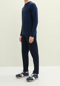 Mörkblå långärmad skjorta i texturerad tyg, ihop med matchande byxor. Svarta och vita sportskor med dämpad sula och detaljer.