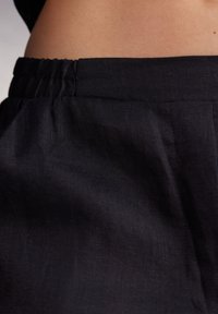 Zwart linnen stof met een gegatherde elastische tailleband, een gladde textuur en een subtiele glans, met plooien en een minimalistisch ontwerp.