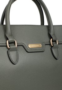 Groene leren handtas met textuur en gouden hardware, heeft dubbele bovenhandvaten en een rechthoekig ontwerp, gedetailleerde stiksels en een logo-tag.