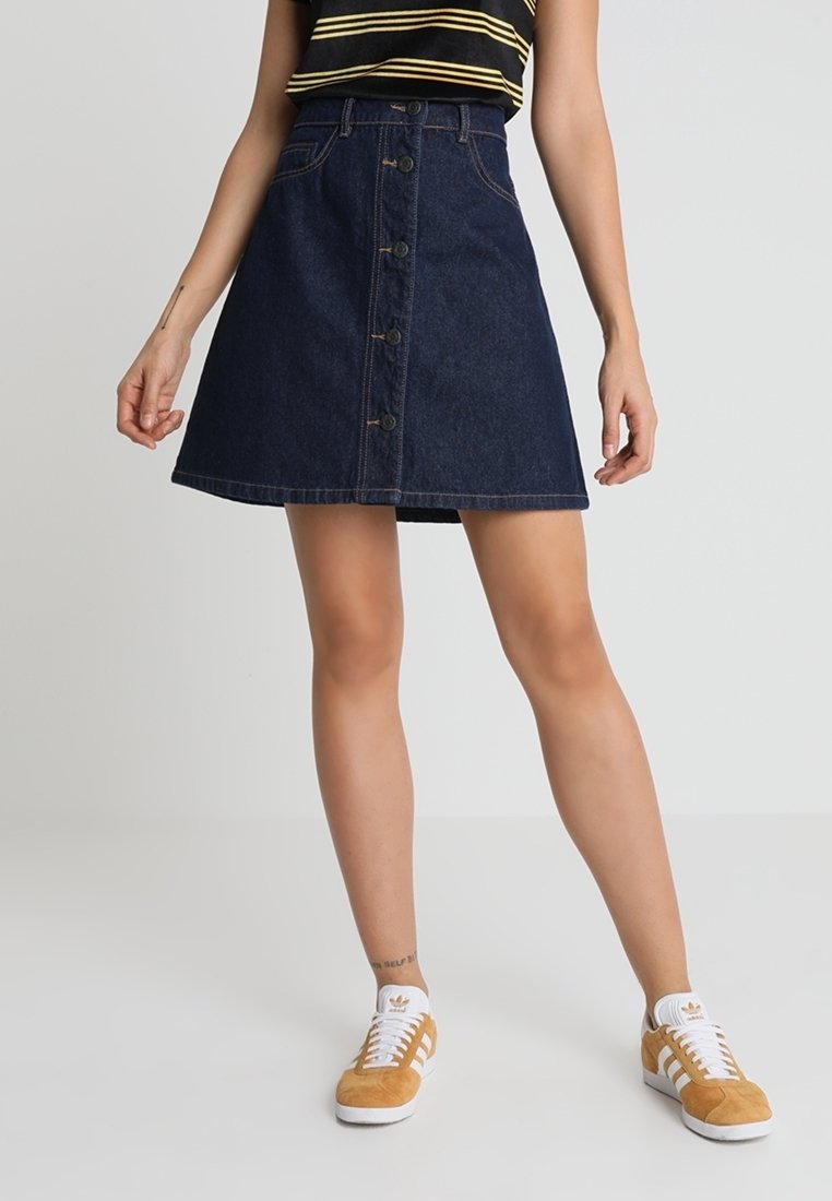 Jeans A-linje kjol, mörkblå, med framknäppning, bältesögglor och sidofickor; matchad med vita och bruna sneakers.