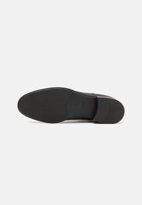 Semelle de chaussure de ville en cuir noir lisse avec une adhérence texturée et le logo en relief "BOSS" au niveau du pied, sur un fond blanc uni.
