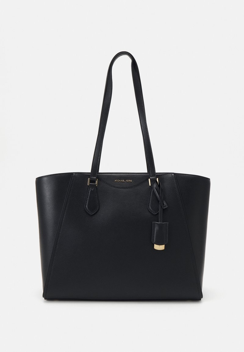 Sac cabas en cuir noir avec longues anses, quincaillerie dorée et étiquette en cuir suspendue, présenté sur un fond clair uni.