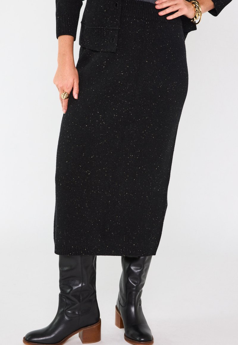 Jupe en maille noire avec des paillettes dorées, taille côtelée, associée à des bottes en cuir noires jusqu'au genou avec un talon épais marron.