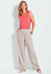 Lichtgewicht koraalkleurige mouwloze top gecombineerd met losse beige broek. De outfit heeft een elastische tailleband en een zachte stofstructuur.