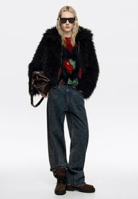 Kurtka z puszystego czarnego futra, kolorowy sweter w wzory, luźne niebieskie dżinsy, brązowe zamszowe buty i ciemne okulary przeciwsłoneczne. Trzyma brązową skórzaną torbę.