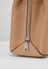 Läcker läderväska i tanfärg med strukturerad yta, prydd med en silverdragkedja och en metalldragflik. Botten har vinklade sömmar för extra hållbarhet.